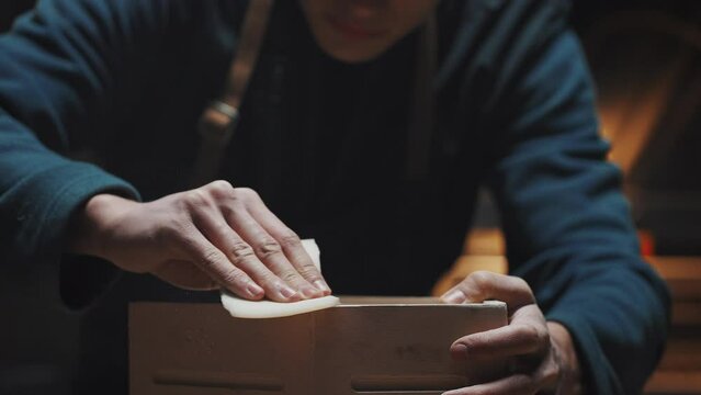 Close portrait of a young attractive Caucasian master carpenter polishing a wooden birdhouse. The guy carefully looks at the results of his work. Carpentry training