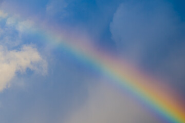 Fototapeta premium Multicolored rainbow after rain among blue sky clouds