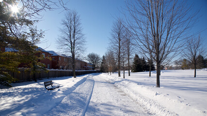 View of a residential district with a footpath in the park with deep snow and a park bench.