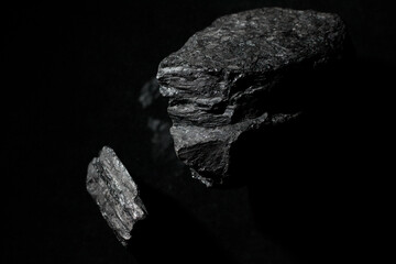 Fototapeta premium Black rocks on a dark background. A wallpaper. Minerals in reflection. A desktop image. Relief stones with reflection. Photo for a desktop and home screen .