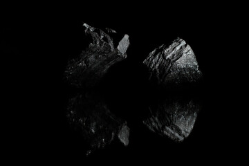 Black textured stones on a dark background lie on a glass surface and, being reflected in it, form unusual figures. A wallpaper for a desktop of a computer or home screen on a mobile phone.