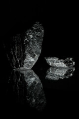 Black textured stones on a dark background lie on a glass surface and, being reflected in it, form unusual figures. A wallpaper for a desktop of a computer or home screen on a mobile phone.