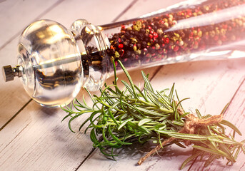 Pepper mill with fresh rosemary on the wooden table. Food cooking background.
