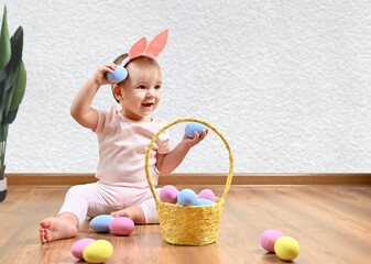 A wonderful little girl with ears on her head smiles sweetly and plays with colored Easter eggs