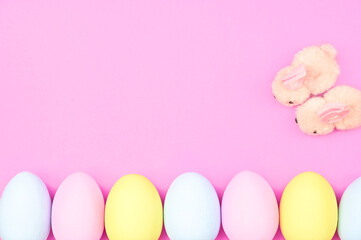 Blue, pink and yellow Easter eggs with cute fluffy bunnies on a pink background with copy space