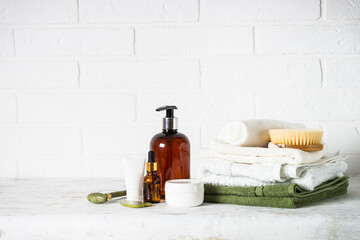 Spa products in white bathroom. Bottle of soap, cosmetics and stack of towels in white bathroom.