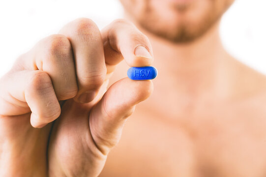 Muscular young man holding Herpes pill isolated on white background.