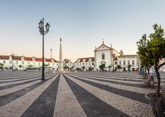 Sunrise in the Marquês de Pombal square in Vila Real de Santo António, Algarve, Portugal, with the obelisk in the center of the square and the old houses and church in the background.