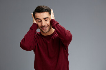 man holding his head with his eyes closed smile posing gesture with hands red sweater Gray background