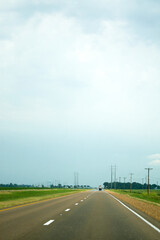 Power lines running alongside a wide, flat two-lane highway under a grey cloudy sky.  Image has concept of road trips and has copy space
