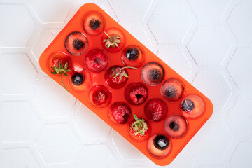 Frozen berries in ice cubes in red silicone tray or mold. Top view.