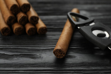 Cigars and guillotine cutter on black wooden table, closeup