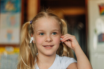 portrait of a smiling child, listening to music in white headphones, dancing, fooling around at home. beautiful girl listens to an audio fairy tale in headphones. generation alpha