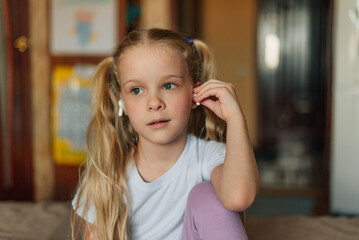 portrait of a smiling child, listening to music in white headphones, dancing, fooling around at home. beautiful girl listens to an audio fairy tale in headphones. generation alpha