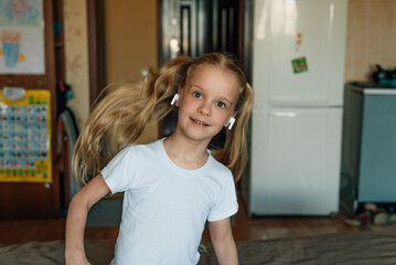 Fototapeta na wymiar portrait of a smiling child, listening to music in white headphones, dancing, fooling around at home. beautiful girl listens to an audio fairy tale in headphones. generation alpha