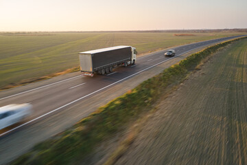 Aerial view of blurred fast moving semi-truck with cargo trailer driving on highway hauling goods in evening. Delivery transportation and logistics concept