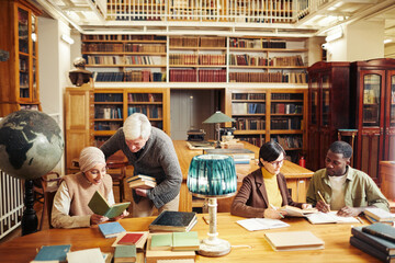 Warm toned portrait of diverse group of people studying at table in classic college library, copy...