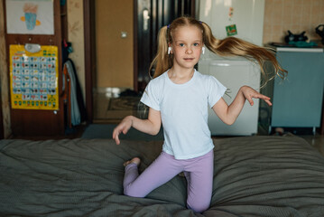 portrait of a smiling child, listening to music in white headphones, dancing, fooling around at home. beautiful girl listens to an audio fairy tale in headphones. generation alpha
