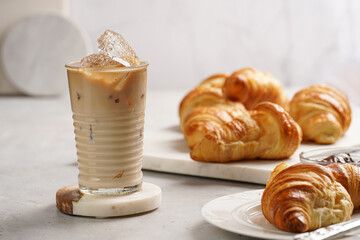 a glass with milk coffee and ice cubes, and freshly baked croissants on marble plate, brown...