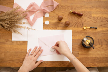 Cropped photo of woman hands making greeting envelope craft, decorate with pink ribbon and...