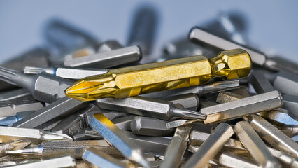 Big golden cross screwdriver bit on silvery bits heap of various sizes and types. Close-up of slot...