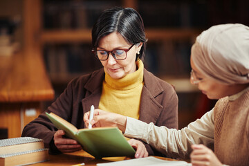 Warm toned portrait of two female adult students reading books while preparing for exam in college...