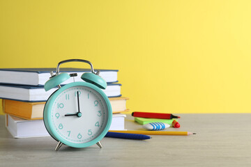 Turquoise alarm clock and different stationery on white wooden table against yellow background,...