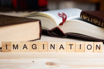 Word IMAGINATION written with wooden blocks, next to books on a table.
