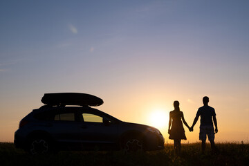 Fototapeta na wymiar Happy couple standing near their car at sunset. Young man and woman enjoying time together travelling by vehicle