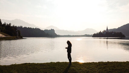 Silhouette of a young woman at sunrise on Lake Bled with famous Slovenian church in Lake Bled,...