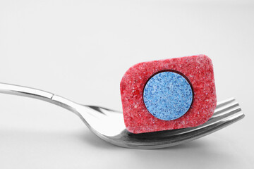 Fork with dishwasher detergent tablet on light background, closeup