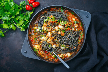 Obraz na płótnie Canvas Traditional Italian spaghetti al nero di seppia with baby squid ink in tomato sauce served as top view in a cast iron pan on a rustic board