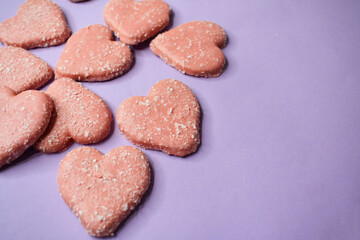 Cookies in the form of pink hearts with coconut flakes on a lilac background