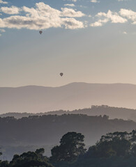 Two hot air balloons float over the Yarra Valley at sunrise