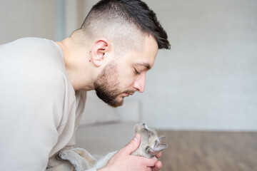 portrait of cute cat with close eyes and handsome bearded guy. Handsome young man is cuddling his...