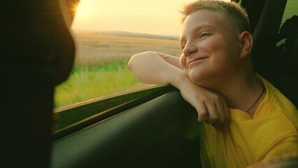 Happy child boy rides in car, looks out car window, dreams. Boy is smiling at passenger in car....