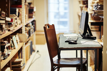 Side view shot of librarian workplace with bookshelves in public library, copy space