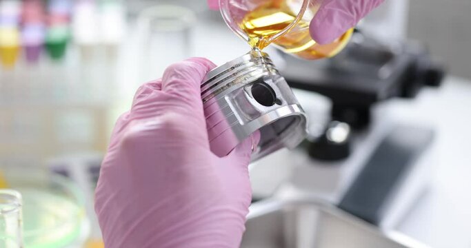 Scientist in rubber pink gloves holds automotive part and pours lubricating oil