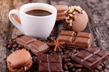cup of coffee with chocolate, macaroons  and coffee beans on wooden background 