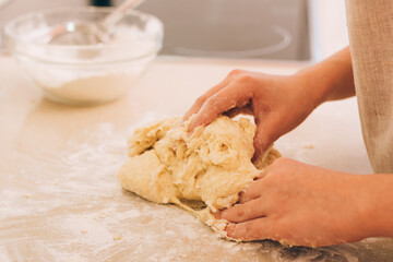 The hands of a young girl are kneading dough for baking on kitchen table. Daily household chores in kitchen.