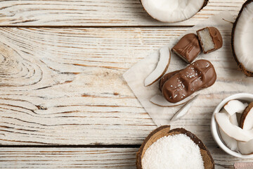 Delicious milk chocolate candy bars with coconut filling on white wooden table, flat lay. Space for text