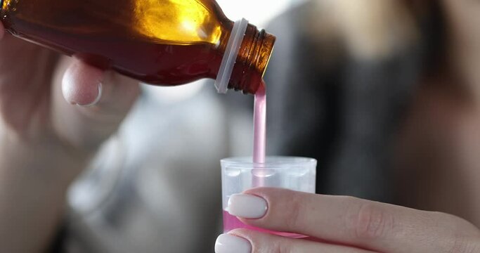 Woman pours cough syrup into measuring cup closeup