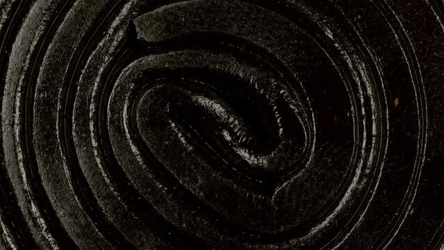 Extreme macro view with rotation of a licorice gummy candy spiral shaped. Dark chewy sweets. Candy texture pattern close up.