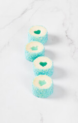 Festive Mousse cream cakes in the form of round sushi with jelly pigeon and heart, sprinkled with blue coconut shavings. Light background