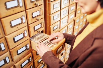 Close up of female librarian searching for book in library catalogue cabinet, copy space
