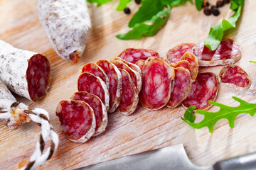 Sliced Catalan sausage Fuet on wooden table with arugula and black pepper - obrazy, fototapety, plakaty