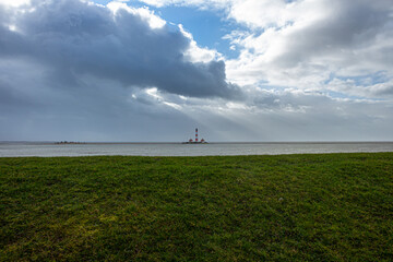Fototapeta na wymiar Der große Leuchtturm von Westerhever steht nach einer Sturmflut bei schönem Wetter und Sonne mitten in den Wellen der Nordsee.