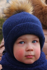A little boy in winter clothes and a warm hat on the street.