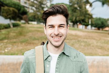 Trendy handsome young student man with backpack smiling at camera while standing at campus college