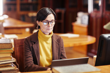 Warm toned portrait of female librarian using laptop while working with book catalogue